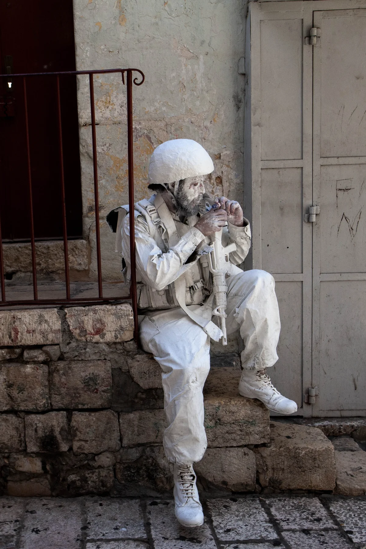 An Israeli soldier dressed in white sits on stone steps, holding a rifle.