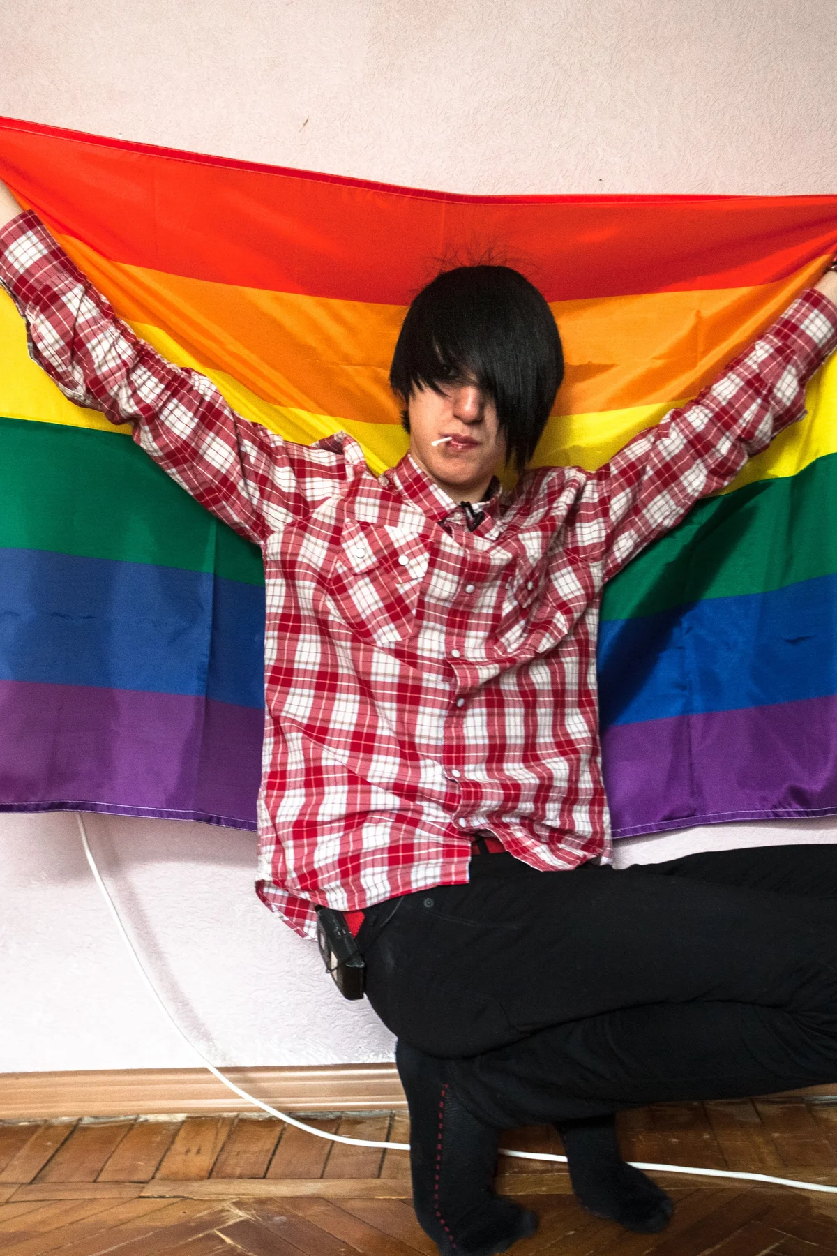 A seated person holds a rainbow flag behind their shoulders.