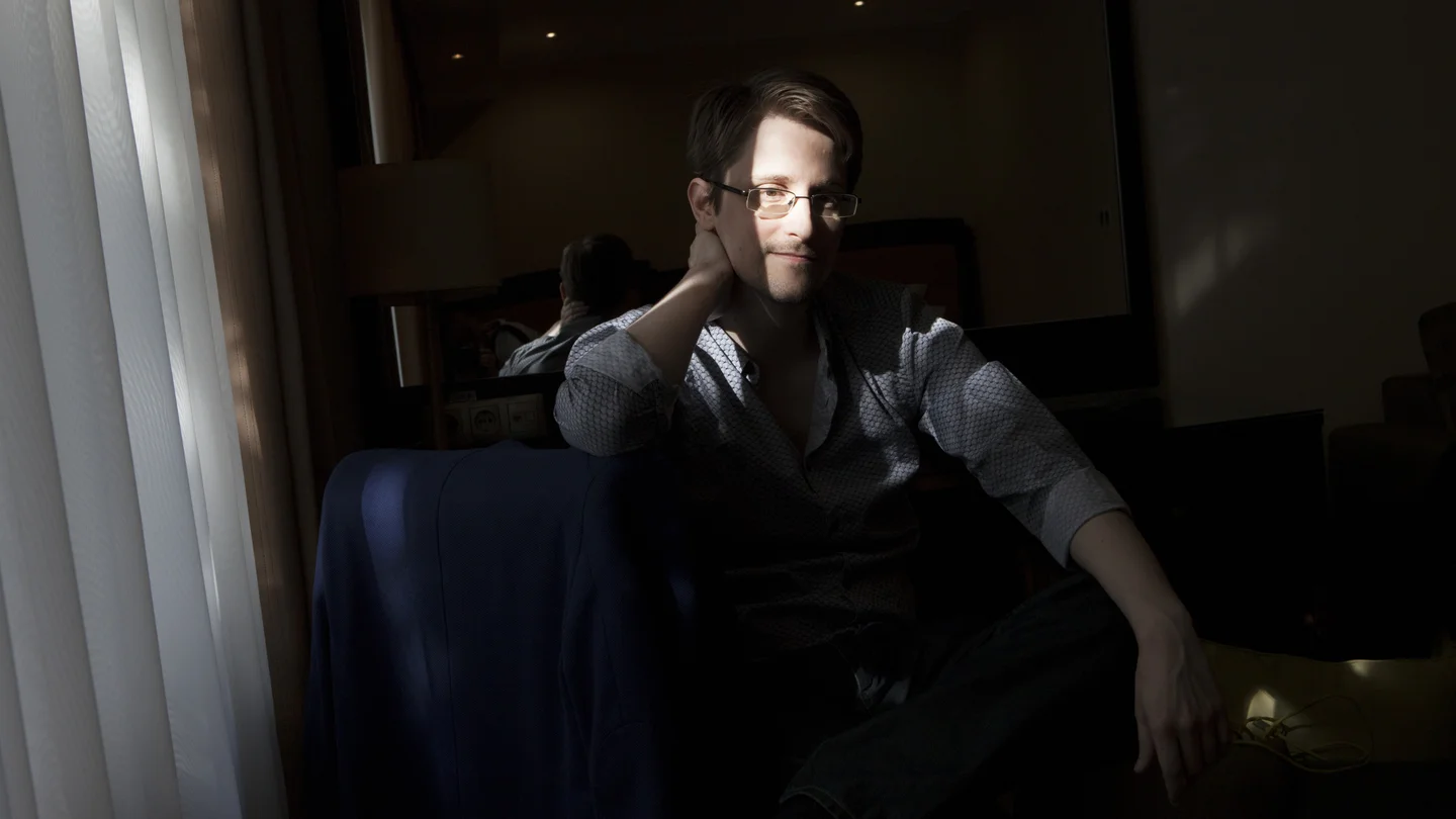 Edward Snowden seated beside a window in a dimly lit room in Moscow.