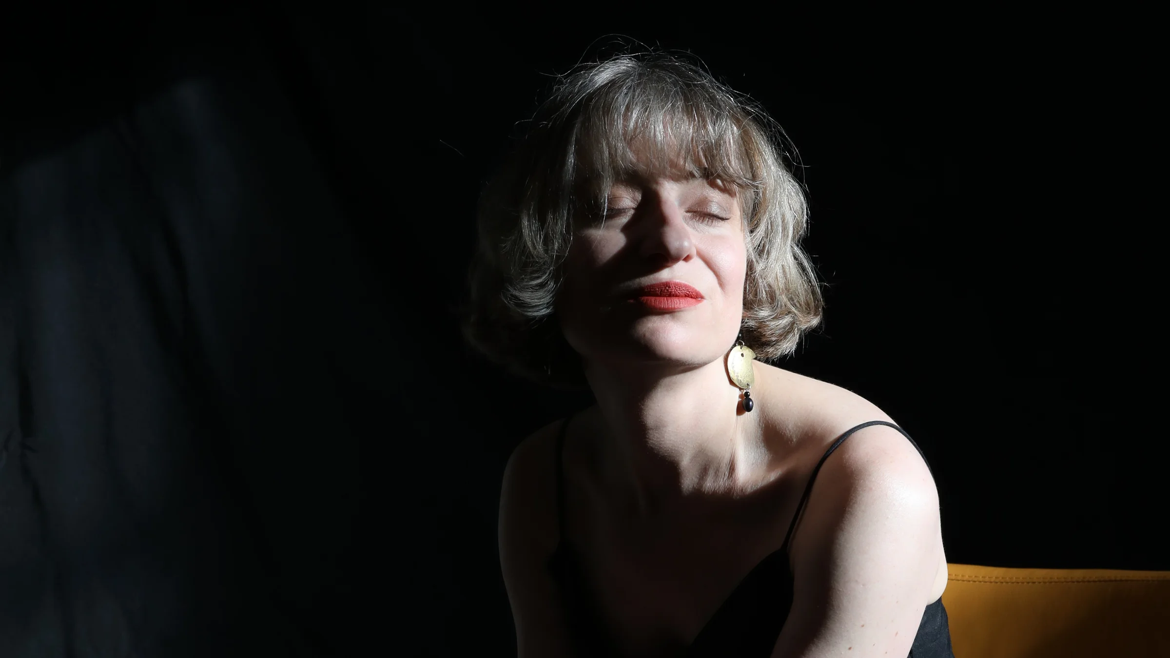 Filmmaker Olga Kravets with her eyes closed, her face lit against a dark background.