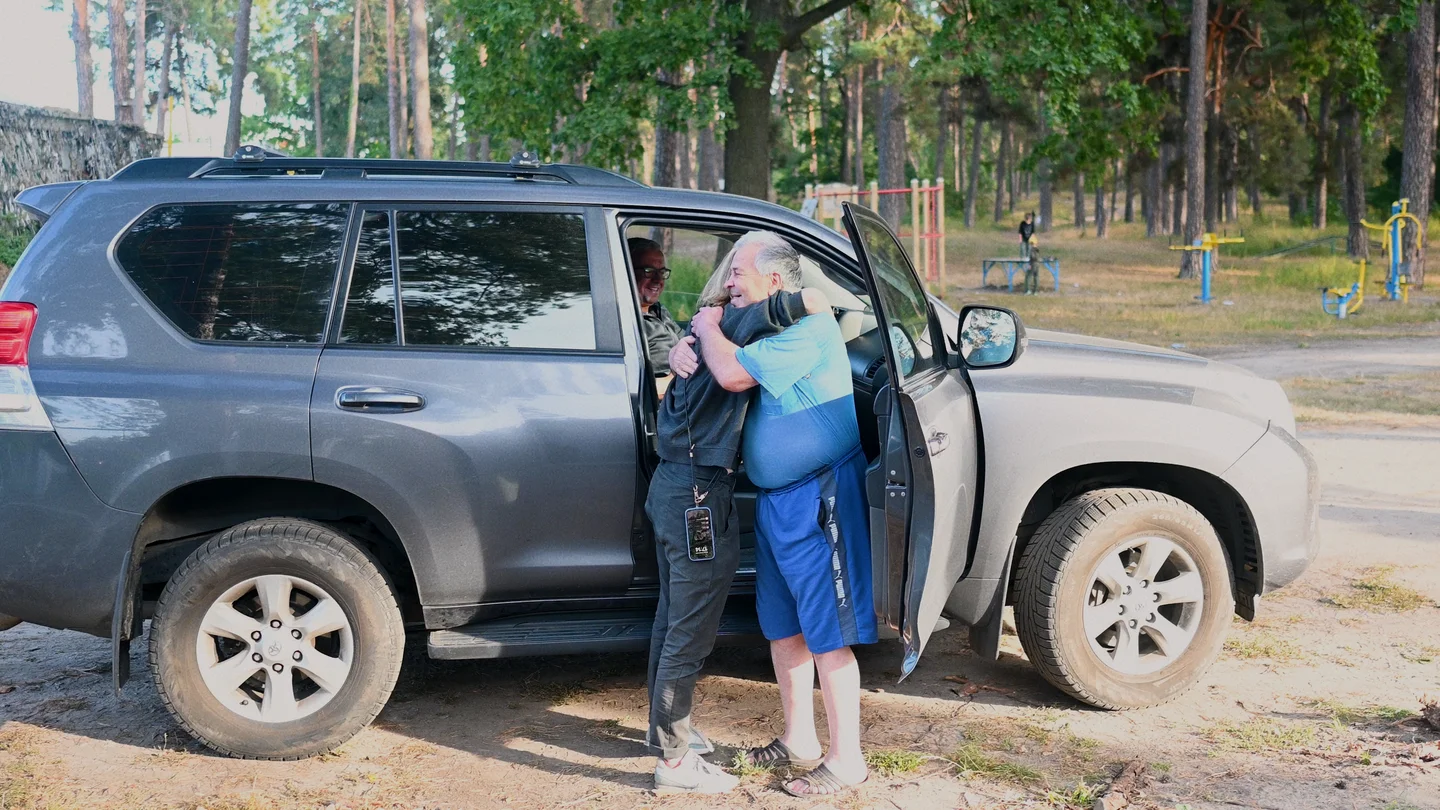 Olga Kravets embraces her Ukrainian uncle next to the open door of an SUV near a wooded park in Kyiv outskirts.