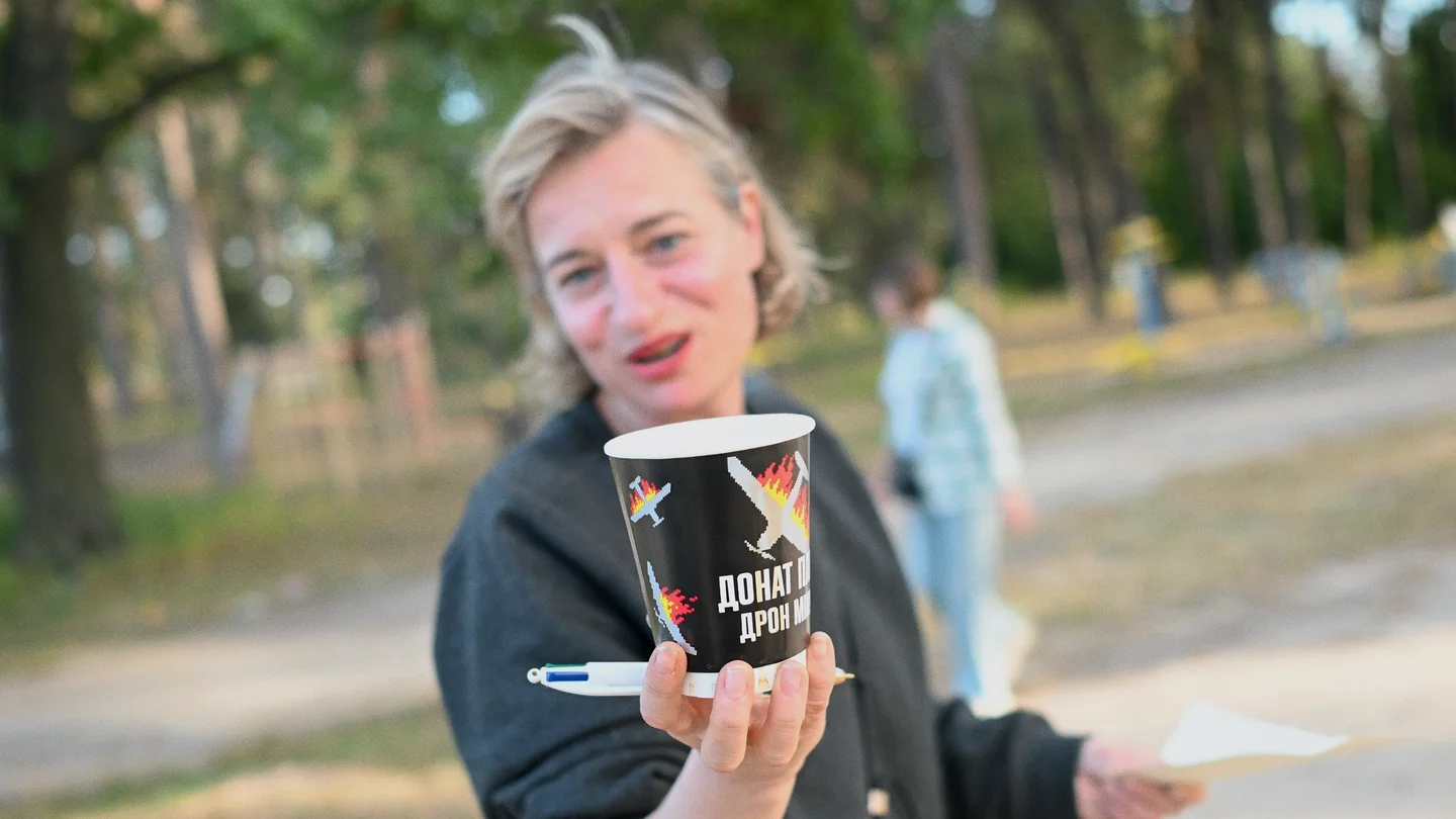 A woman holds up a black donation cup decorated with birds and Ukrainian lettering.